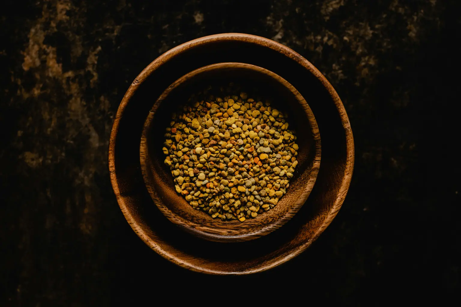 polen de abeja natural en grano en cuenco de madera sobre fondo oscuro