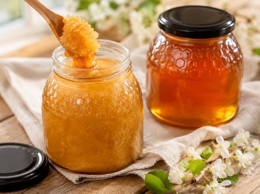 Tarro de miel cristalizada natural con textura granulada y cuchara de madera