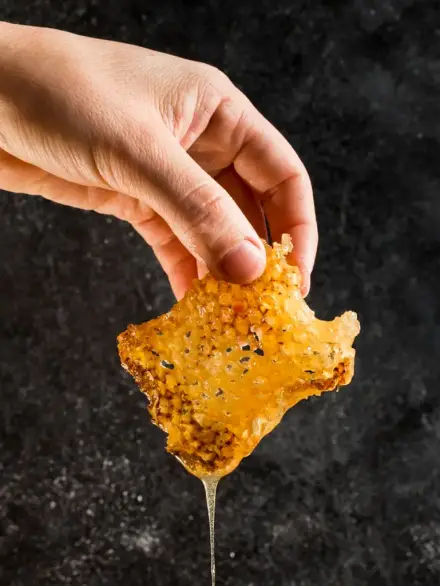 mano sujetando panal de miel natural con miel goteando sobre fondo oscuro